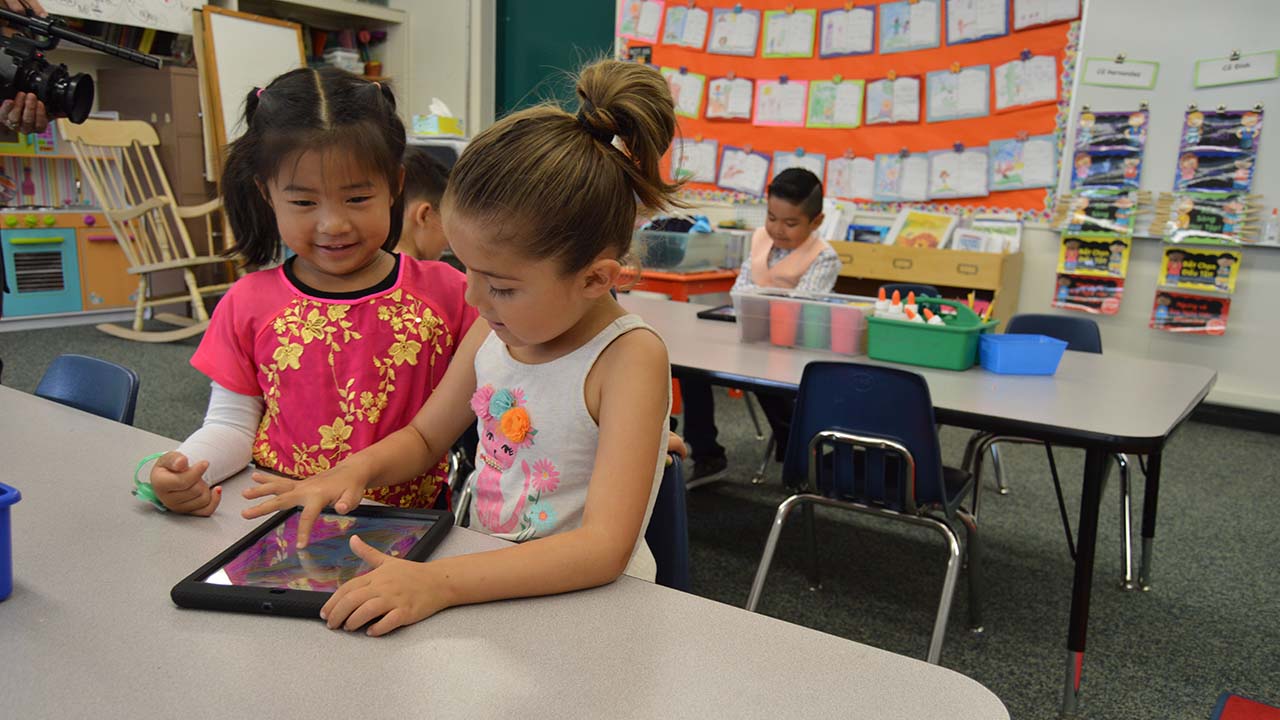 two students sitting at desk working together on an Ipad